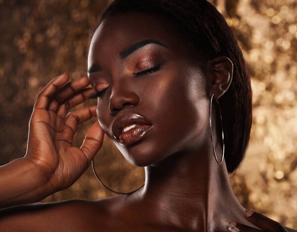 Fashion studio portrait of an extraordinary beautiful african american model with closed eyes, perfect smooth glowing mulatto skin, bright make up, over golden background