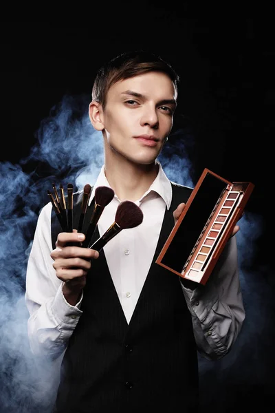 Young male make up artist posing with make-up brushes and shadow — Stock Photo, Image