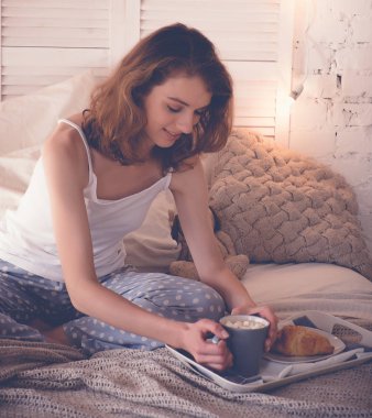 Evde yatakta kahve içen güzel bir kadın.
