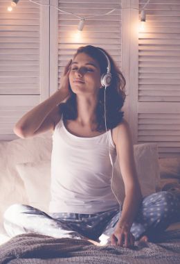 Genç kadın yatağında dinleniyor, müzik dinliyor.