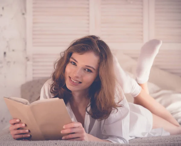 Estilo de vida y el concepto de la gente: Mujer joven acostada en la cama mientras lee — Foto de Stock
