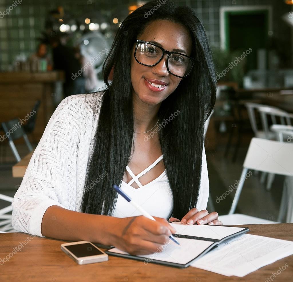 Portrait of beautiful young black woman sitting at cafe and writ