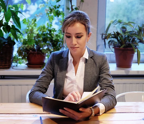 Młoda bizneswoman siedzi przy stole w kawiarni i czyta — Zdjęcie stockowe