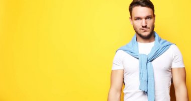 Gündelik giyinen genç adam sarı çantanın üzerinden kameraya bakıyor.