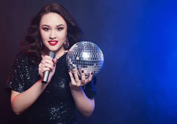 Estilo de vida y el concepto de la gente: mujer con vestido negro, sosteniendo la bola disco y cantando en el micrófono — Foto de Stock