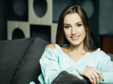 Rahat bir sandalyede oturan ve kameraya bakan sıradan giyinen güzel bir genç kadının stüdyo fotoğrafı.