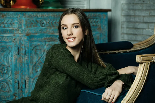 Studio shot of beautiful young woman wearing casual outfit sitting in a big comfortable chair and looking at camera — Stock Photo, Image