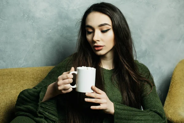 Cantik dan manis. Wanita muda cantik memegang cangkir kopi dan duduk di kursi di rumah. Konsep gaya hidup. — Stok Foto