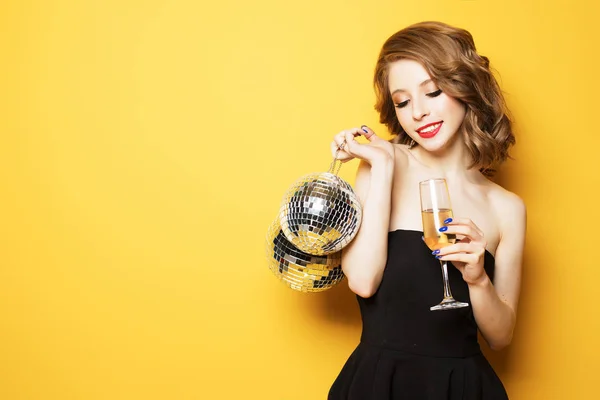 Сексуальная женщина с бокалом белого вина и диско мяч на желтом фоне — стоковое фото