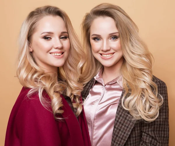 Fashion portrait of two girls, best friends posing indoor on beige background wearing winter stylish coat. — Stock Photo, Image