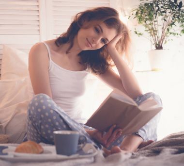 Yatakta kitap okuyan ve kahve içen kız.