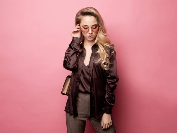 Красивая блондинка в блузке и брюках в очках, держащая сумочку — стоковое фото