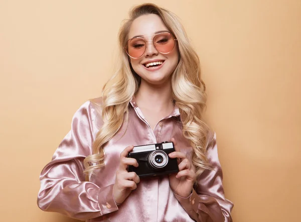 Retrato de uma jovem menina loira sorridente segurando câmera fotográfica isolada em um fundo bege — Fotografia de Stock