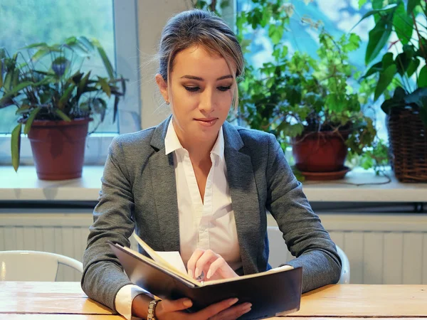 Genç iş kadını kahve dükkanında oturmuş kitap okuyor. — Stok fotoğraf