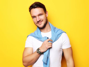 Gündelik giyinen genç adam sarı çantanın üzerinden kameraya bakıyor.