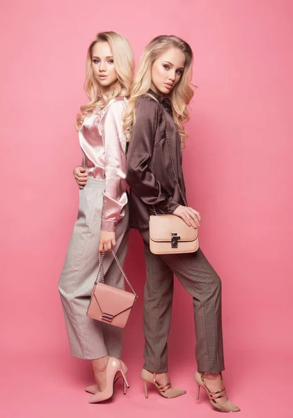 Zwei schöne junge Frauen in lässiger Kleidung posieren vor rosa Hintergrund. — Stockfoto