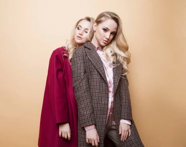Mode porträtt av två flickor, bästa vänner poserar inomhus på beige bakgrund bär vinter elegant jacka. — Stockfoto