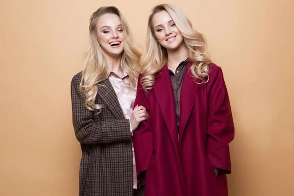 İki kızın moda portresi, en iyi arkadaşlar bej arka planda poz veriyorlar kışlık şık bir ceket giyiyorlar.. — Stok fotoğraf