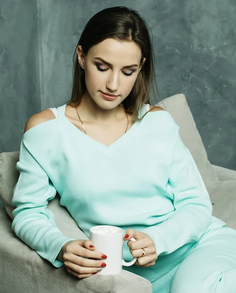 Frumos şi drăguţ. O tânără frumoasă care ține ceașcă de cafea și stă pe scaun acasă. Conceptul de stil de viață . — Fotografie, imagine de stoc