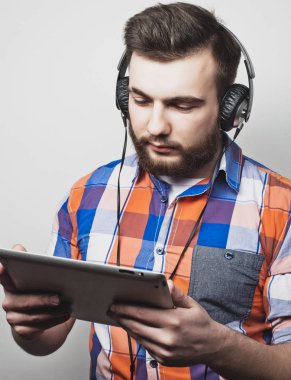 Açık gri arka planda kulaklık takan yakışıklı sakallı bir adamın stüdyo portresi..