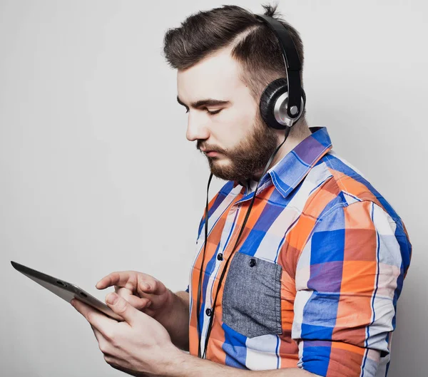 Studio πορτρέτο ενός όμορφου γενειοφόρου άνδρα χρησιμοποιώντας ένα tablet με ακουστικά πάνω από ένα ανοιχτό γκρι φόντο. — Φωτογραφία Αρχείου