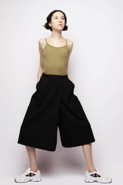   Güzel bir kadın, günlük kıyafetler giyiyor, beyaz bir sırt üzerinde poz veriyor.