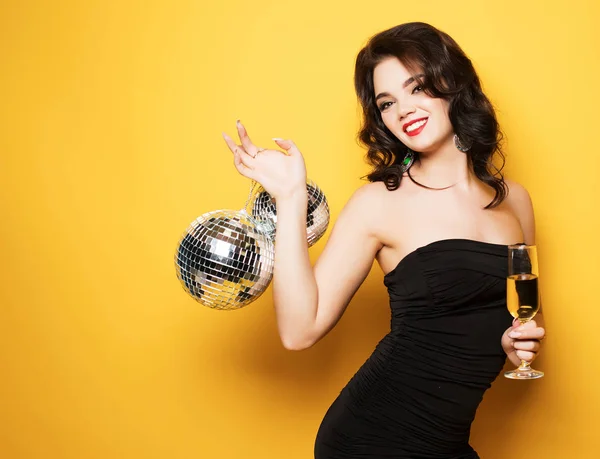 Sexy žena se sklenkou bílého vína a disco koule nad žlutým pozadím — Stock fotografie