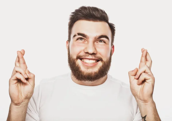 Waiting for special moment. Portrait of young man   keeping fingers crossed  while standing against white background — Stock Photo, Image