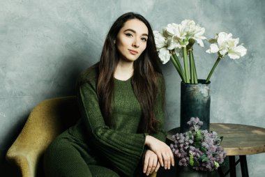 Rahat bir sandalyede oturan ve kameraya bakan sıradan giyinen güzel bir genç kadının stüdyo fotoğrafı.