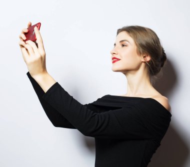 Selfie zamanı. Genç, gülümseyen sarışın kadın beyaz arka planda özçekim yapıyor..