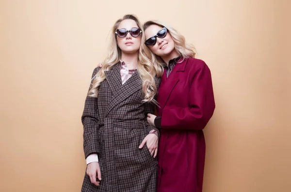 Retrato de moda de duas meninas, melhores amigos posando interior no fundo bege vestindo casaco elegante inverno. — Fotografia de Stock