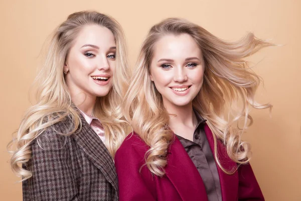 Fashion portrait of two girls, best friends posing indoor on beige background wearing winter stylish coat. — Stock Photo, Image