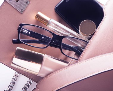 Pembe deri kadın çantası beyaz arka planda kozmetik ve aksesuarlarla açılır..