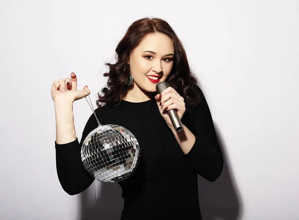 Lifestyle και άνθρωποι έννοια: γυναίκα φορώντας μαύρο φόρεμα, κρατώντας disco μπάλα και το τραγούδι σε μικρόφωνο — Φωτογραφία Αρχείου