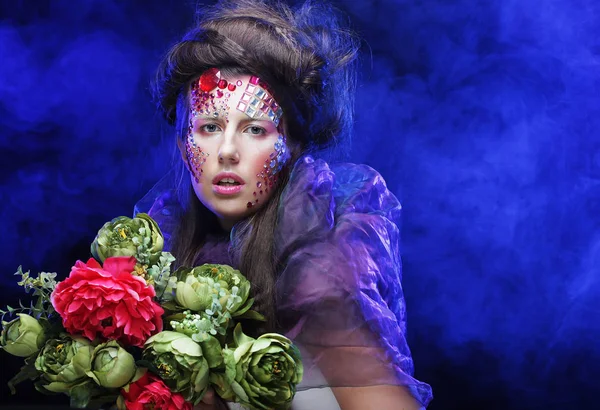 Junge Frau mit kreativem Make-up hält Blumen in der Hand — Stockfoto