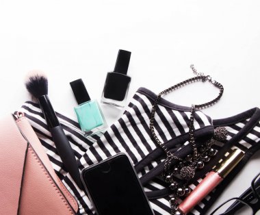 Gözlükleri, temeli, dudak parlatıcısı, pudrası, fırçası, el çantası, beyaz üst görüşe izole edilmiş çizgili gömleği olan stilize kadın bezi. Metin için yukarıdan gelen kadın aksesuarları.