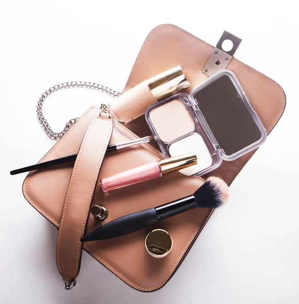 Posa piatta di borsa donna in pelle rosa aperta con cosmetici, accessori e smartphone su sfondo bianco — Foto Stock