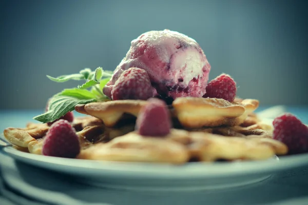 Waffles com sorvete de framboesa e framboesas frescas, decorados com hortelã sobre fundo de madeira azul — Fotografia de Stock