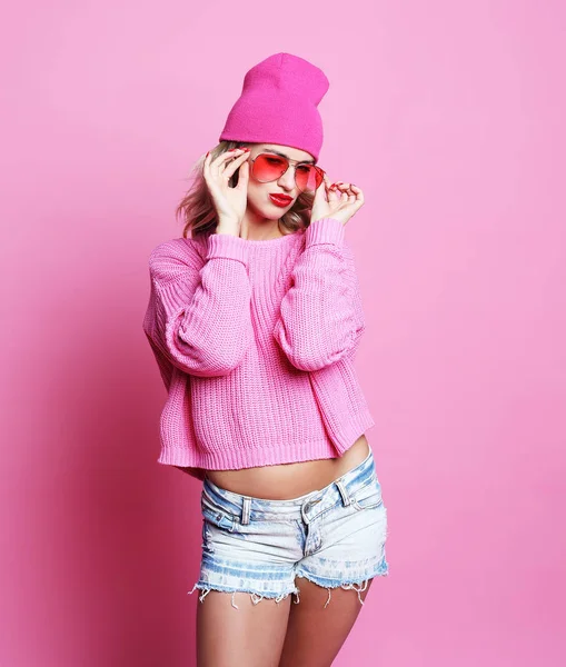 Cooles, fröhliches Mädchen mit leuchtend roten Lippen trägt moderne Strickmütze und rosa Pullover. Hipster-Stil. Jugendmode. rosa Hintergrund. — Stockfoto