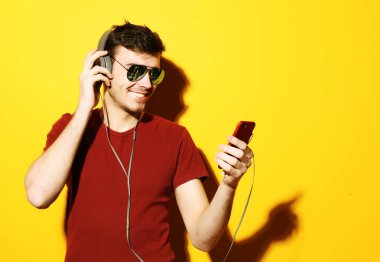Kulaklık takan ve cep telefonu tutan genç bir adam..
