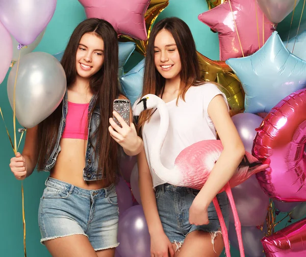 Ready for party. Two girls in stylish summer outfit , paper glasses and air balloons having fun and celebrate birthday.Blue background.