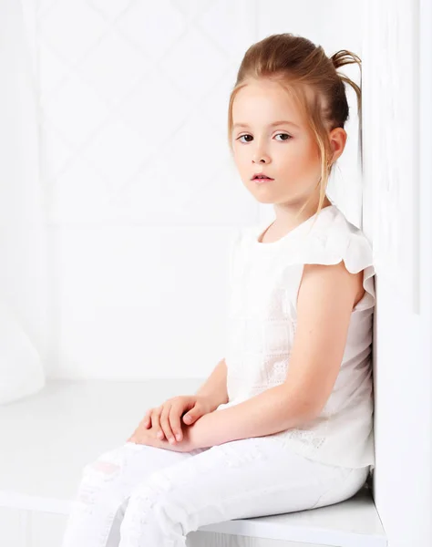 Moda dla dzieci. Piękna dziewczyna zamyślony poważne Blondynka w białych strojach siedzi i pozowanie. — Zdjęcie stockowe