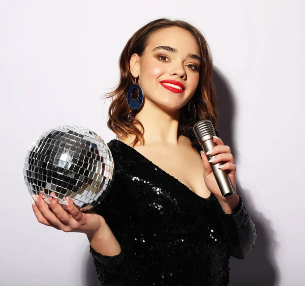 Молодая женщина в черном платье, держит диско мяч и поет в микрофон — стоковое фото
