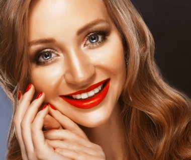 Güzel model kız uzun kıvırcık saçlı ve kırmızı dudaklar. Kırmızı manikür çivi üzerinde. Güzellik ve estetik bakım. Koyu arka plan.