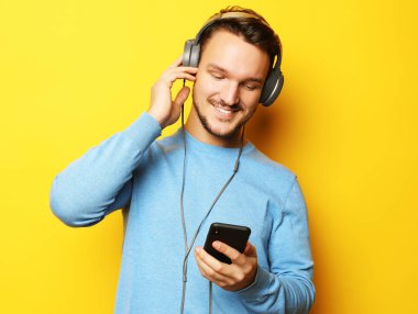 Yaşam tarzı ve insan konsepti: Sarı arka planda kulaklıkla müzik dinleyen mutlu genç adam