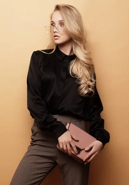 Young beautiful woman in a brown blouse and pants holds a handbag and posing on a beige background. — Stock Photo, Image