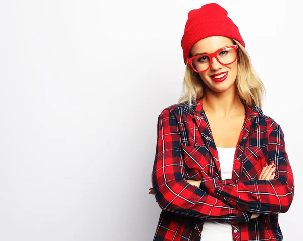 Retrato de mujer rubia hipster bastante joven con maquillaje sexy brillante y gafas, con elegante camisa a cuadros urbana y sombrero rojo, fondo blanco . — Foto de Stock