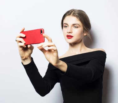 Selfie zamanı. Genç, gülümseyen sarışın kadın beyaz arka planda özçekim yapıyor..