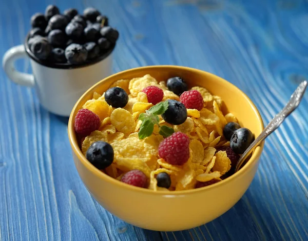 Cornflakes with berries raspberries and blueberries on blue wooden background. — Stock Photo, Image