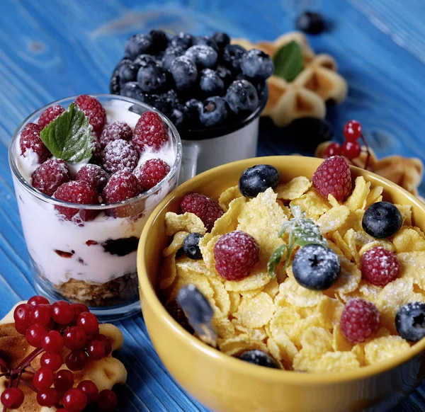 Café da manhã saudável com flocos de milho, bagas, waffle e leite em fundo azul . — Fotografia de Stock